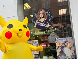 En stor Pikachu-figur foran Halmes Hules butiksvindue med Pokémon-kort og butikkens logo.